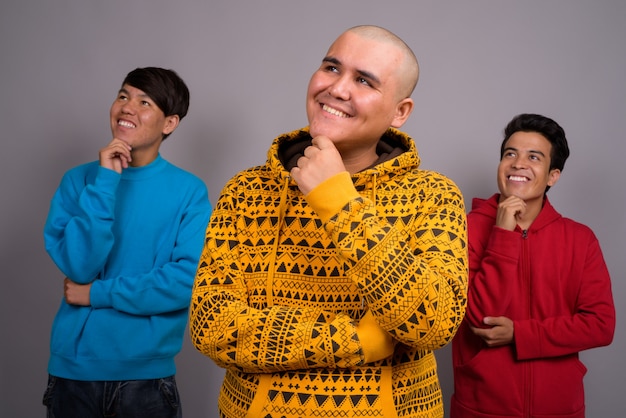 회색 벽에 따뜻한 옷을 입고 세 젊은 아시아 남자