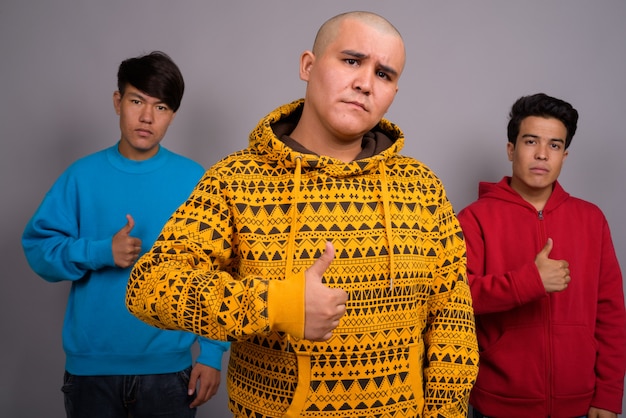 three young Asian men wearing warm clothing against gray wall