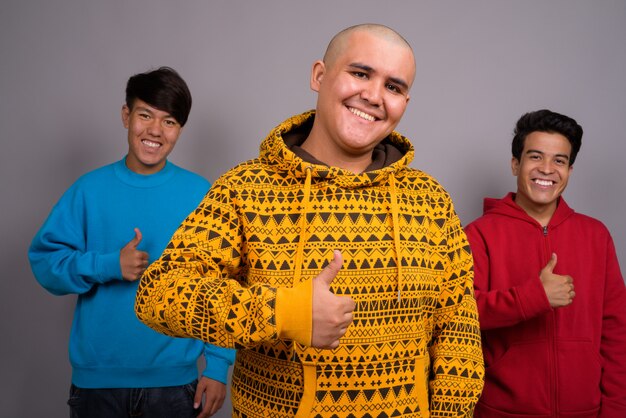three young Asian men wearing warm clothing against gray wall