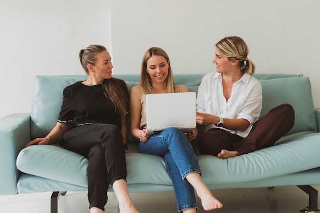 Три молодые привлекательные женщины дома на диване разговаривают, глядя на ноутбук