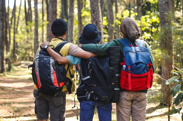 Трое молодых друзей-туристов в рюкзаках стоят, обняв друг друга за плечи.
