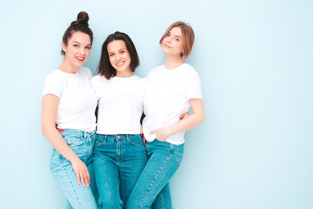 three young beautiful smiling hipster female in trendy same summer white t-shirt and jeans clothes