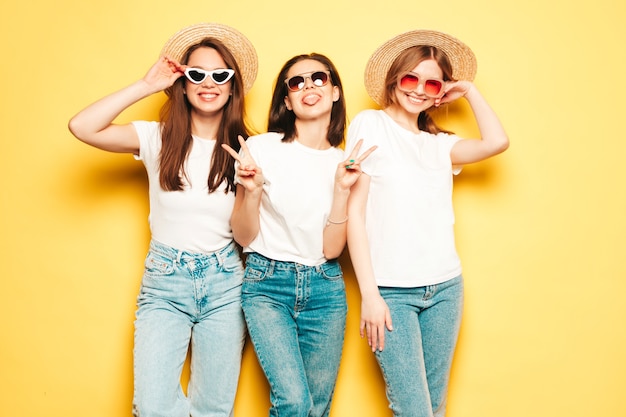 Tre giovani belle donne hipster sorridenti in t-shirt bianca estiva alla moda e vestiti di jeans