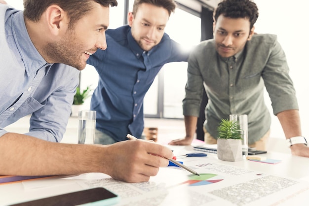 Three young businessmen leaning at table and working at project together, business teamwork concept