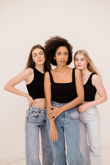 Three young caucasian and african women in casual clothes look at camera on white background