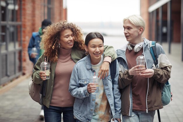 Three young cheerful friends in casualwear having drinks on their way home