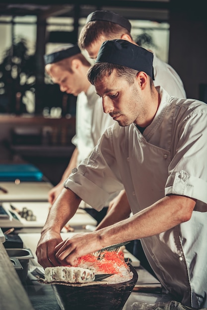 写真 白い制服を着た3人の若いシェフが、彼らが取り組んでいるレストランで調理済みの料理を飾ります