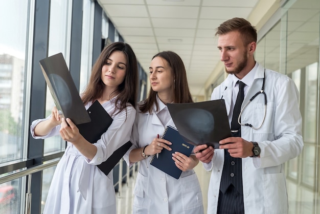 Three young doctors discusses the results of an MRI scan of the patient's head in modern hospital hallway. Health