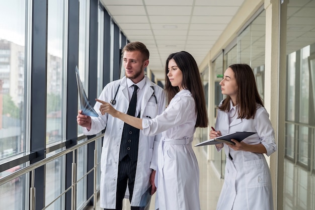 Three young doctors discusses the results of an MRI scan of the patient's head in modern hospital hallway. Health