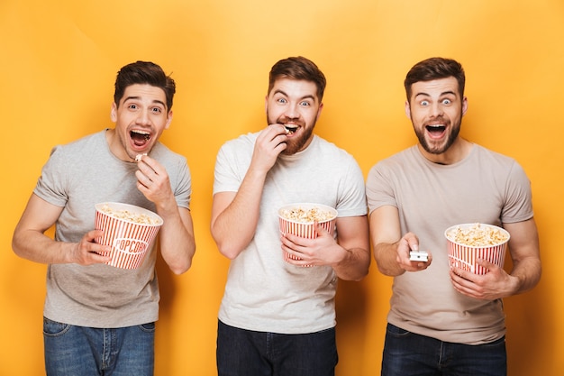 Three young excited men eating popcorn