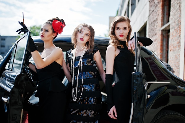 Three young girl in retro style dress near old classic vintage cars. 