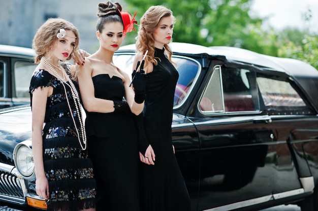 Three young girl in retro style dress near old classic vintage cars. 