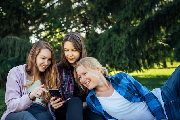 写真 本とスマートフォン、女性の友情の概念と緑の草の上に座っている3人の若い女の子