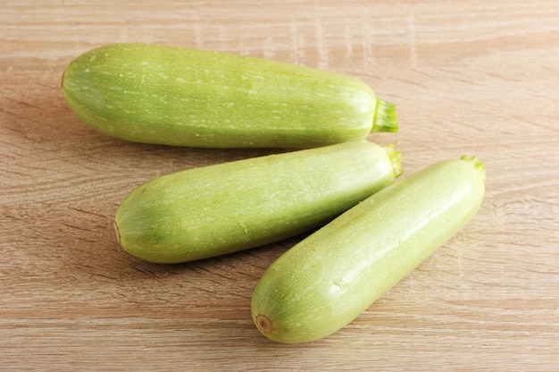 Three young green zucchini on wooden background