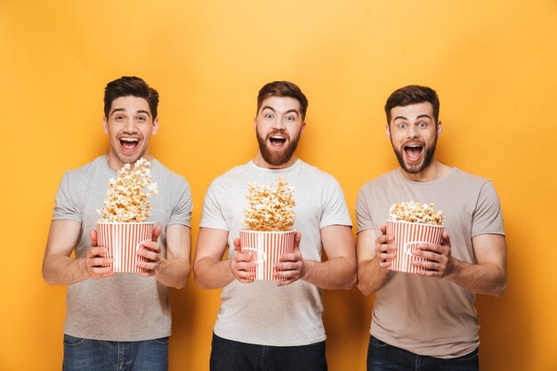 Three young happy men eating popcorn