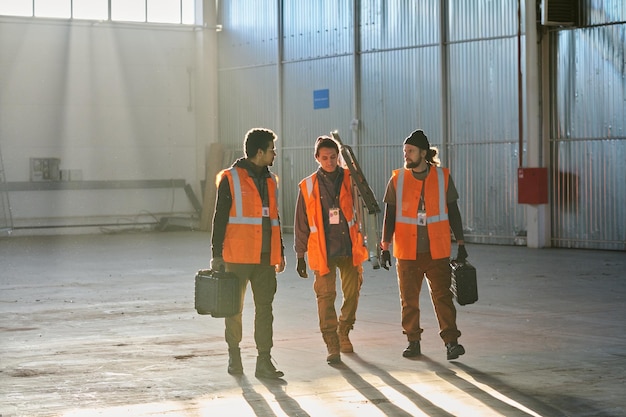 Three young male engineers of warehouse carrying toolboxes and stepladder