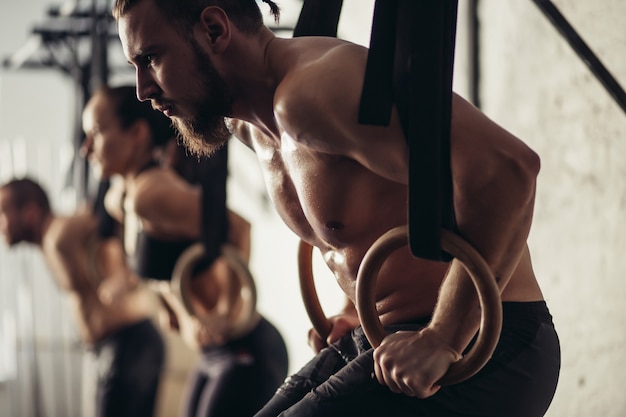 Photo three young male and female adults doing pull ups on rings