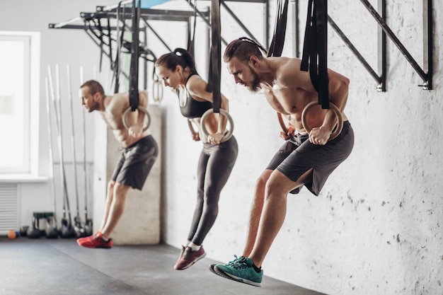 Three young male and female adults doing pull ups on rings