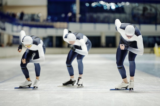 Three young male ice skaters sliding along rink on arena