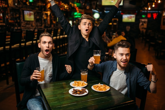 Трое молодых людей празднуют игровую победу в спорт-баре, счастливую дружбу футбольных фанатов