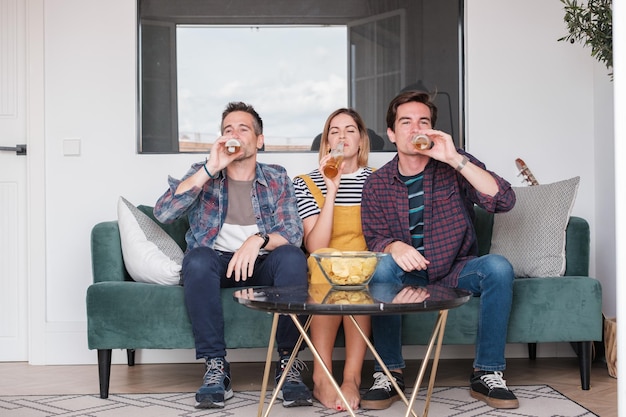 Three young people enjoying a leisurely afternoon together having a beer watching a movie