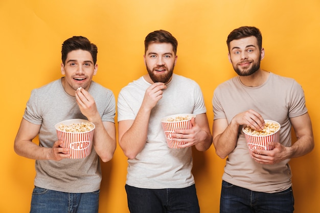 Three young smiling men eating popcorn