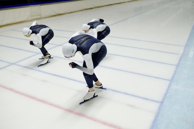 Three young sportsmen bending while sliding along ice rink