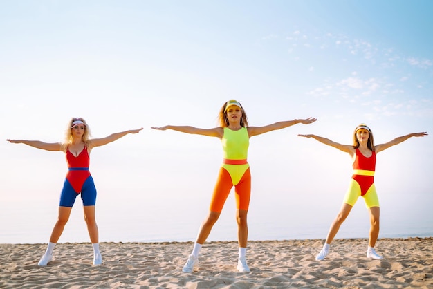 Three young woman dancer dancing in bright swimsuits on the beach Sport fitness active life