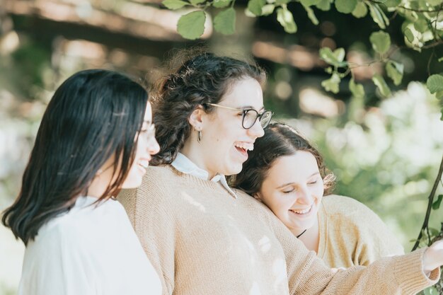 Three young woman having fun and laughing without looking at camera during a sunny day, friendship and care concepts