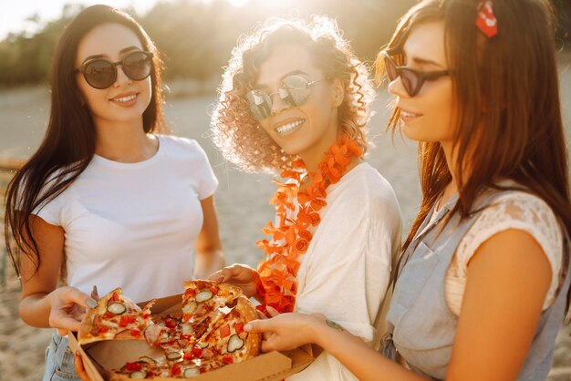 Foto tre giovani donne che trascorrono del tempo insieme in spiaggia facendo un picnic mangiando pizza