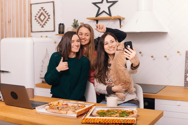 3人の若い女性が自宅のキッチンでピザを食べてクリスマスを祝っています。