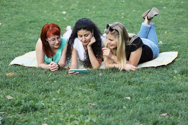 Tre giovani donne sono sdraiate sull'erba e guardano nello smartphone