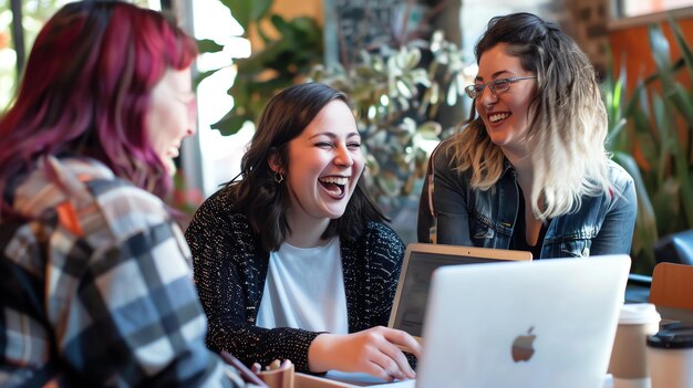 Photo three young women are sitting at a table in a coffee shop laughing and talking they are all wearing casual clothes and have their laptops open