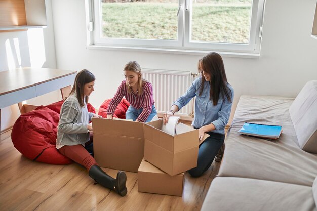 Three young women unpacking cardboard boxes in a room