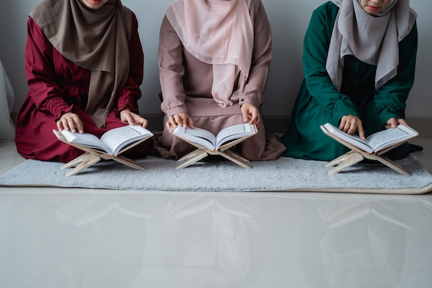 Three young women wearing hijabs read the holy book of the Al-Quran together