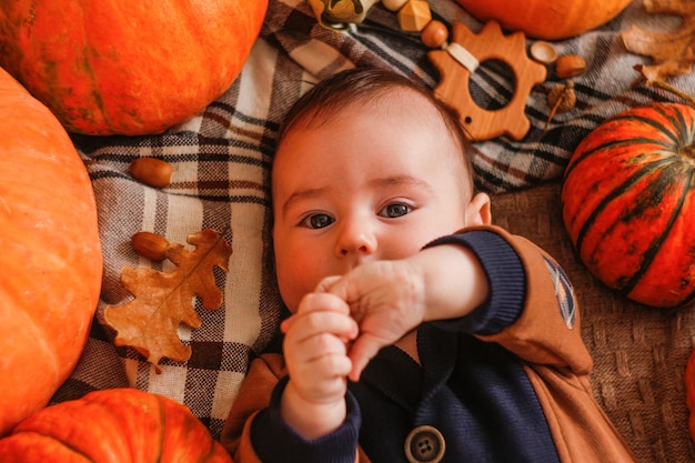 Un bambino di tre mesi si trova con le zucche su una coperta ragazzo carino in posa sullo sfondo di una zucca