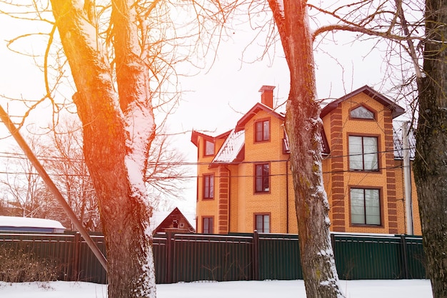 Threestory orange brick house behind dark green fence and snowcovered trees winter sunny day