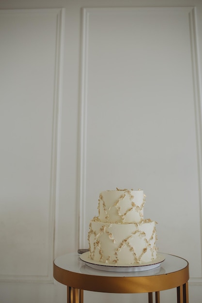 Трехъярусный белый свадебный торт, украшенный цветами из мастики на белом деревянном столе Изображение для меню или каталога кондитерских изделий с копией пространства