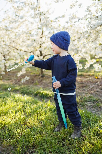 Трехлетний мальчик бежит по цветущему саду с мыльными пузырями Веселый эмоциональный ребенок гуляет по парку Мыло для детей