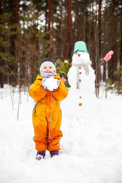 Threeyearold girl in orange jumpsuit with snowman outside in winter