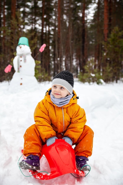 Threeyearold girl in orange jumpsuit with snowman outside in winter