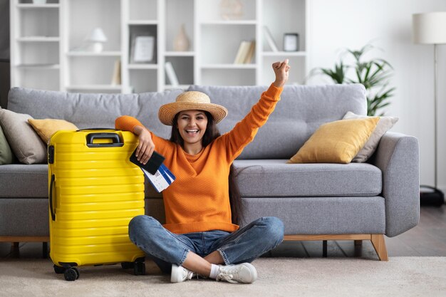 Thrilled indian woman with suitcase passport and tickets home interior