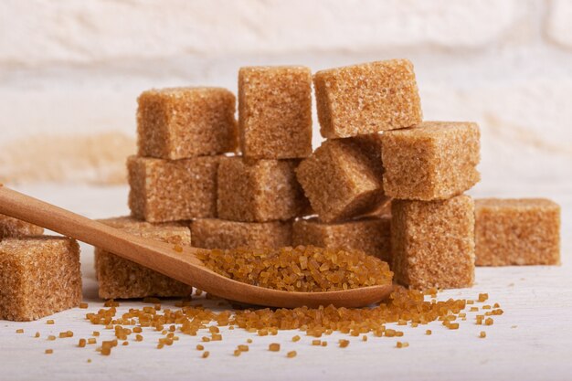 Photo throsy sugar in a wooden spoon against the background of brown sugar cubes