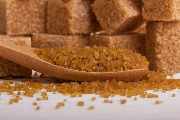 Throsy sugar in a wooden spoon against the background of brown sugar cubes