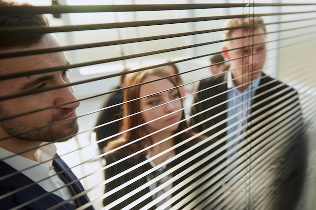 Сквозь жалюзимолодые коллеги по бизнесу смотрят в окно офиса