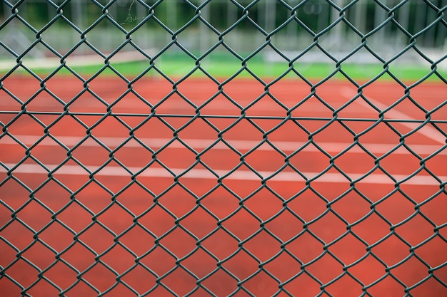 Photo through the chain link fence a blurred tennis court beckons enticing players to the game and sporting competition