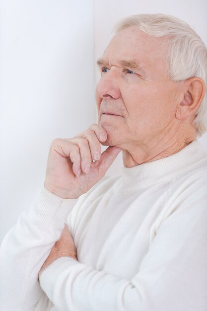 Through the prism of past years. Handsome senior man holding hand on chin and looking away