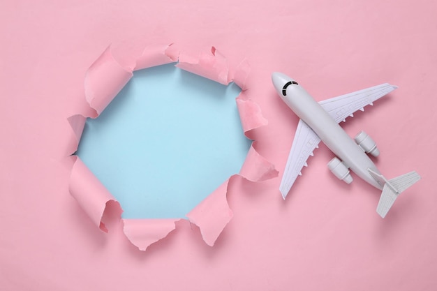 Through a torn hole and air plane on a bluepink pastel
background travel concept pastel color trend minimalism