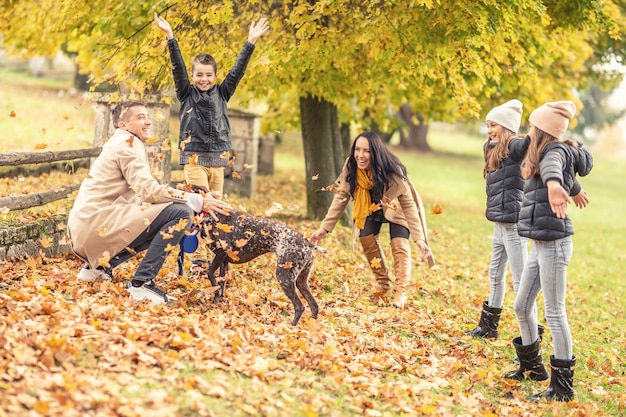 Throwing leaves in the air and playing with a dog outdoors by a family of five.