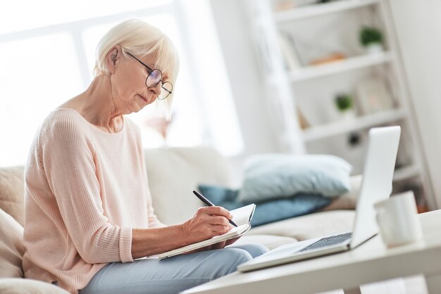 Thuis bezig. Mooie oudere vrouw die iets opschrijft